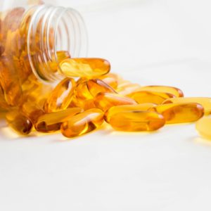 Close-up of fish oil capsules spilling from a bottle on white background.
