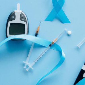Flat lay of a glucose meter, syringe, and blue ribbon symbolizing diabetes awareness.